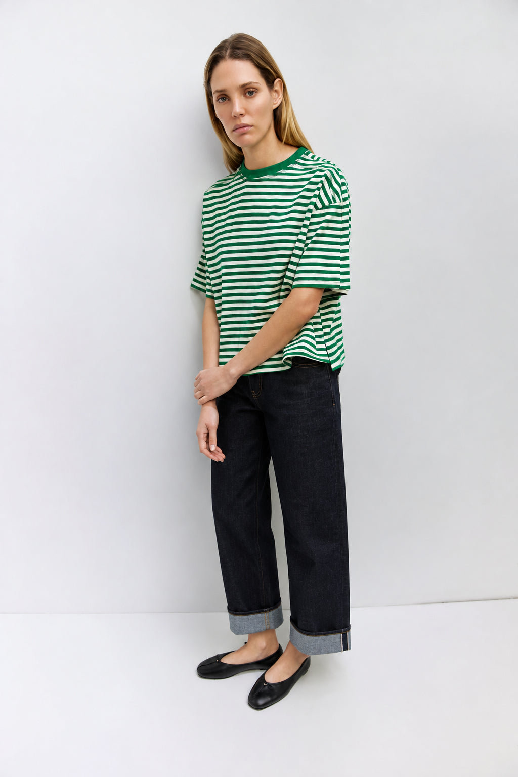 Woman wearing a green and white striped shirt and dark jeans against a white background