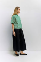 Woman wearing a green and white striped shirt and black pants against a white background