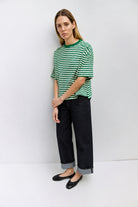 Woman wearing a green and white striped shirt and dark jeans against a white background