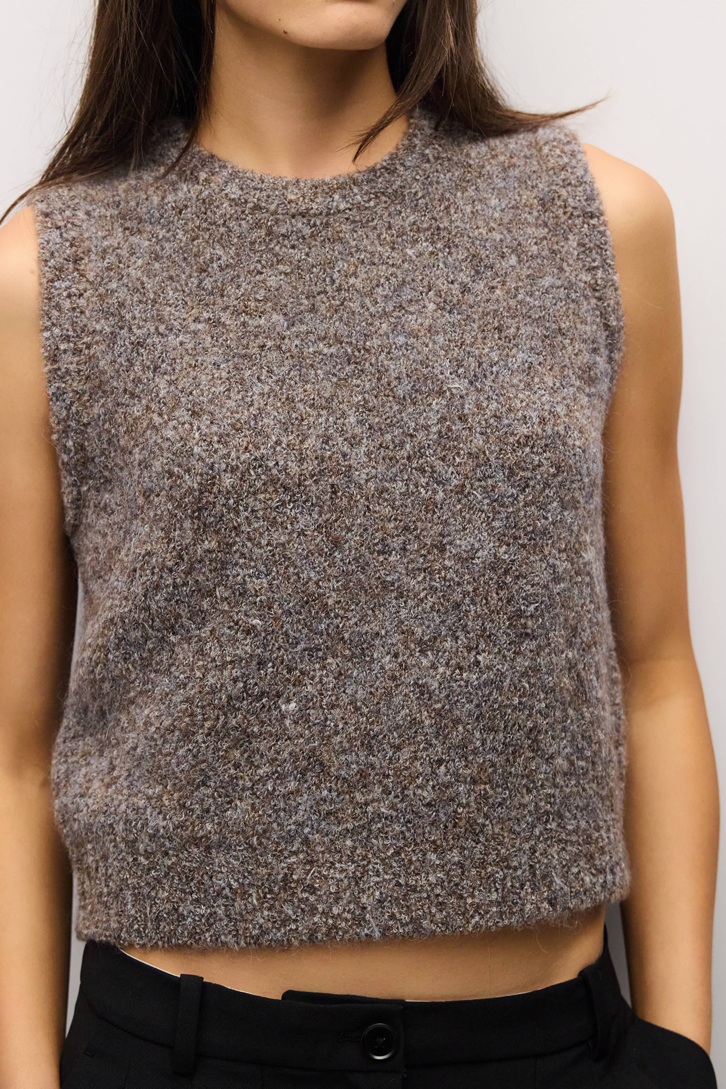 A sleeveless cropped knit sweater vest in a heathered brown and gray melange, worn by a model.