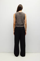 A woman viewed from the back wearing a sleeveless marled gray knit top and black wide-leg trousers, standing against a plain light gray studio background.