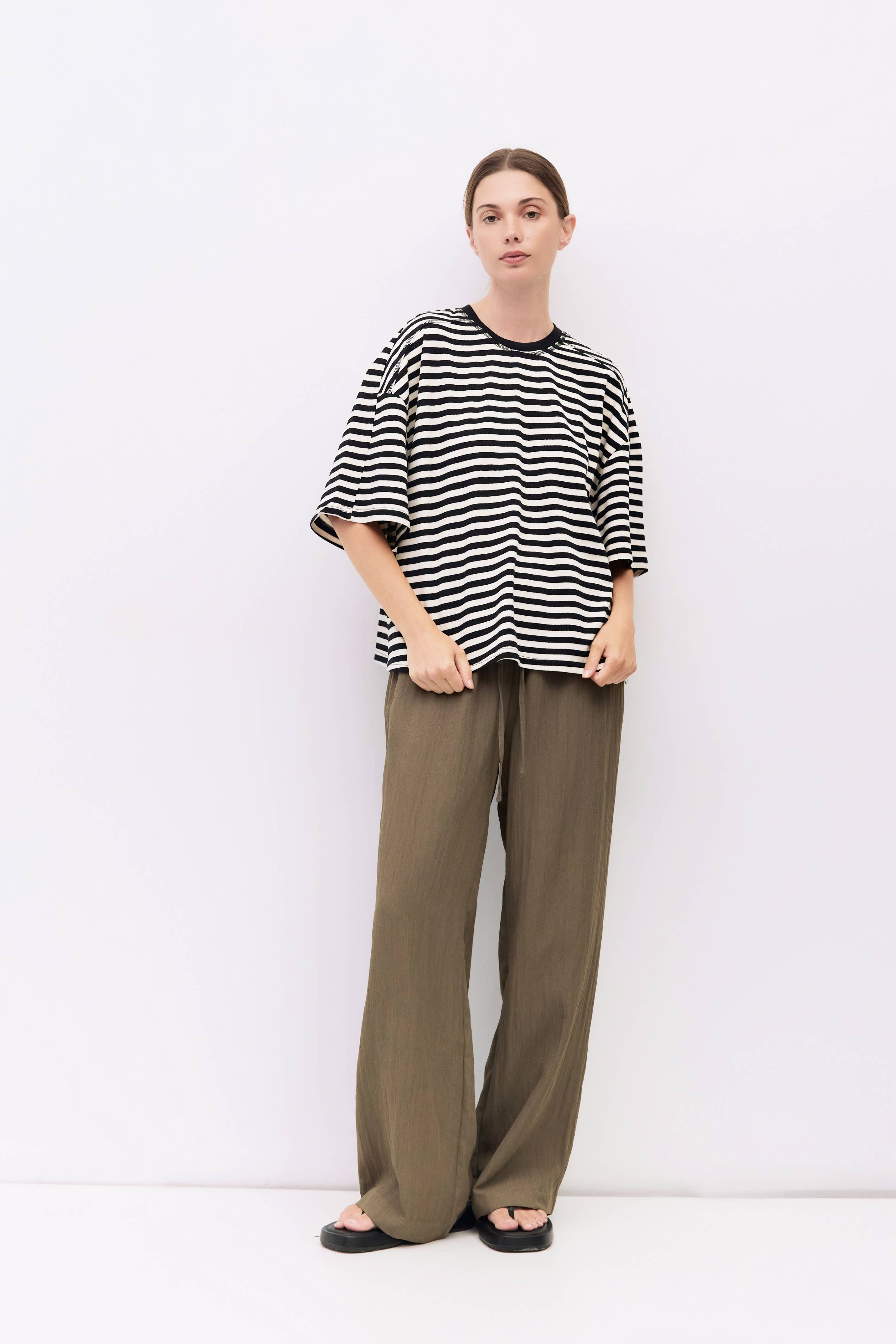 Person wearing a black and white striped shirt and green pants against a white background