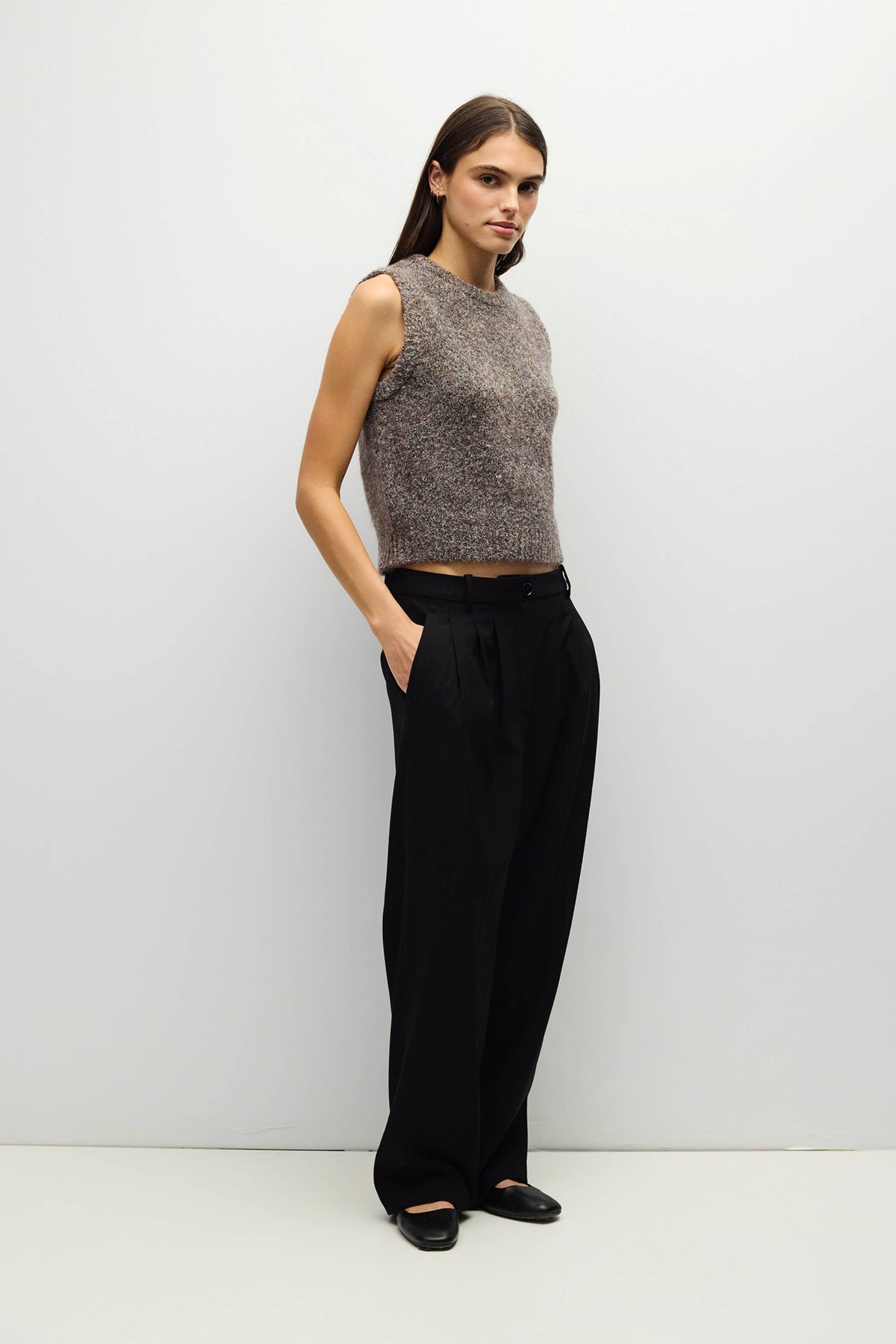 Woman wearing a brown and gray mélange sweater vest and wide-leg pants on a white background