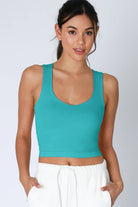 A woman wearing a green racerback crop top and light green denim shorts.